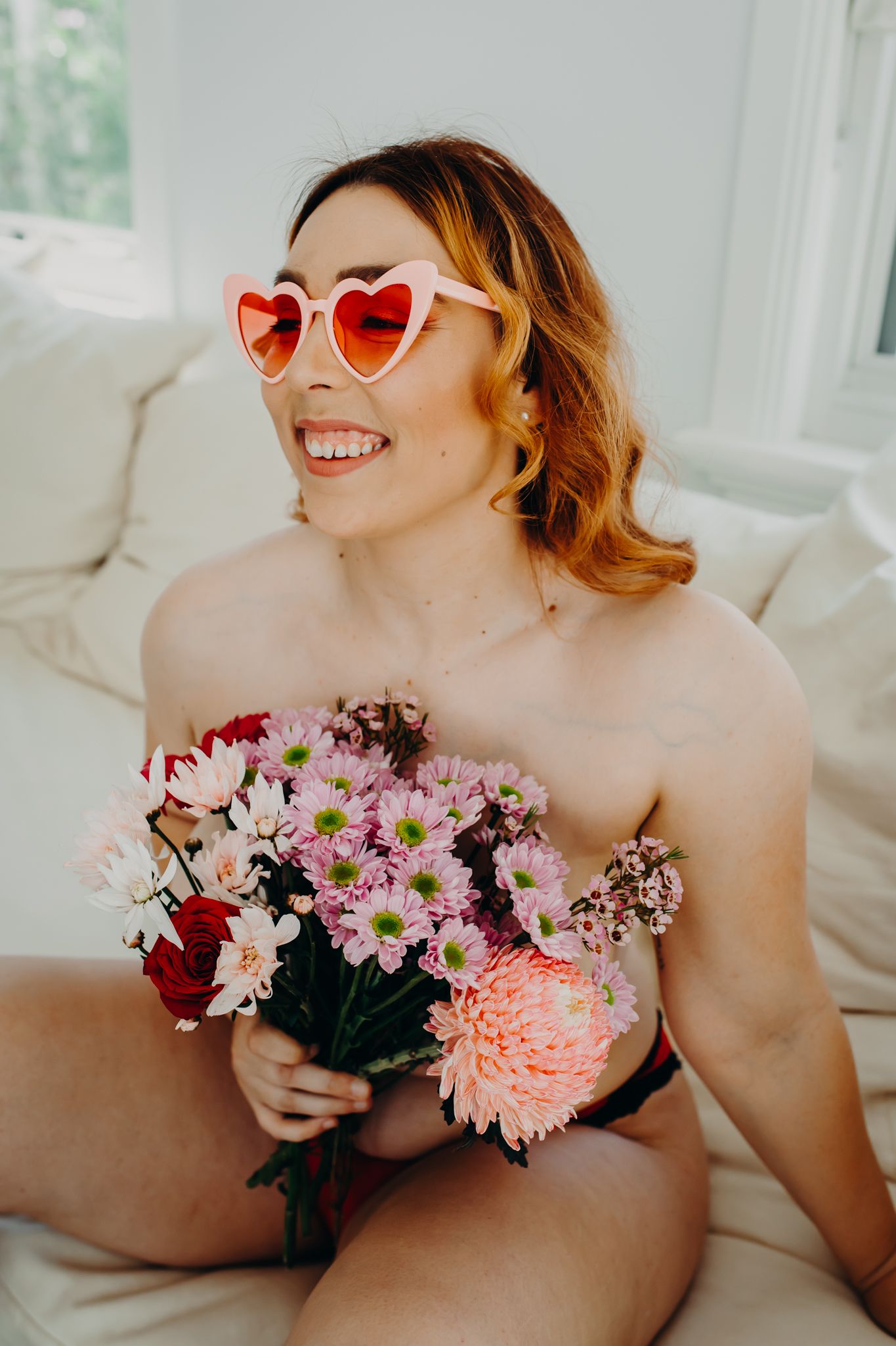 Playful boudoir shot with heart-shaped sunglasses and mixed floral bouquet.