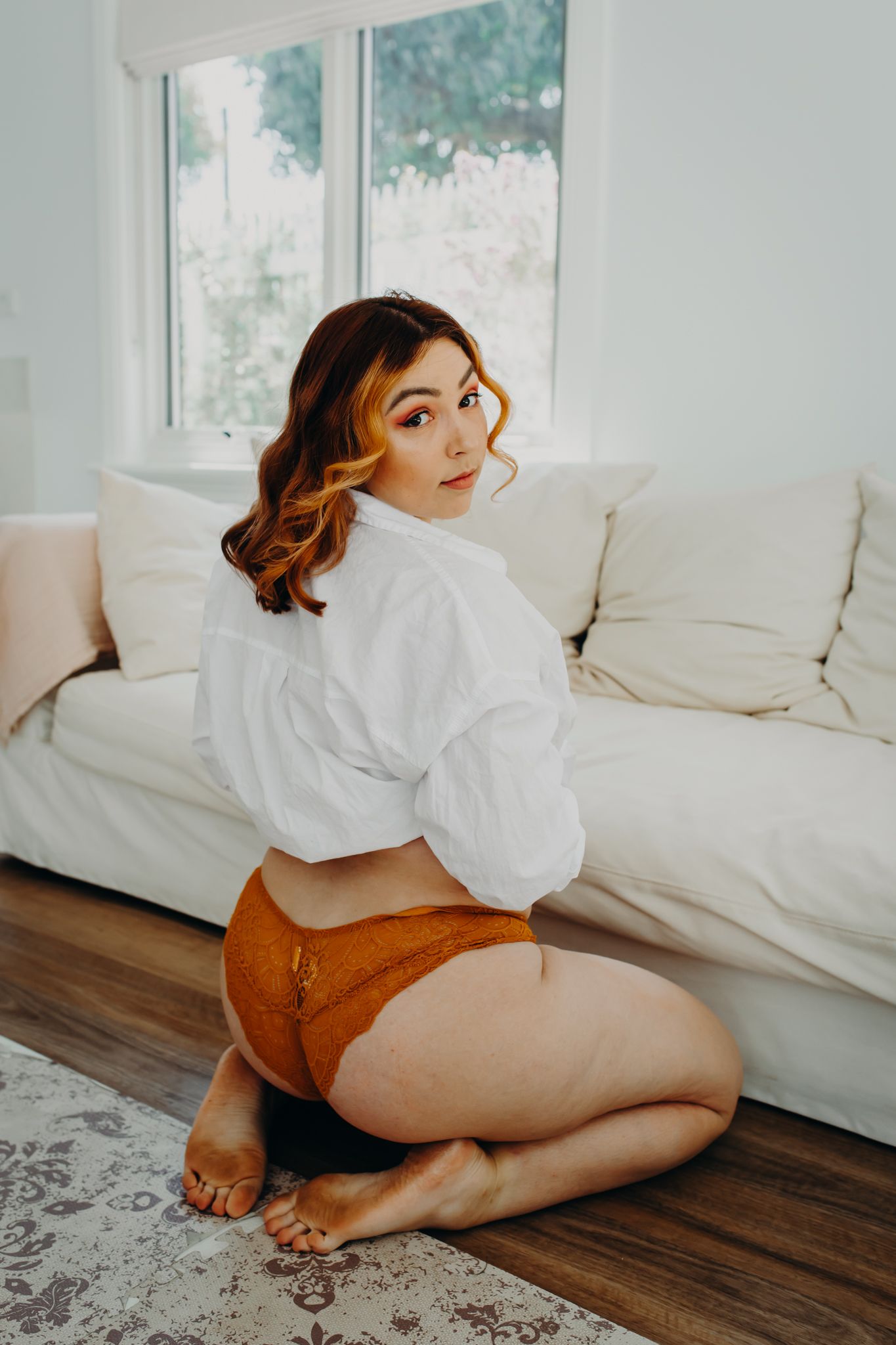 Artistic pose in white button down shirt and copper colored underwear on hardwood floor.