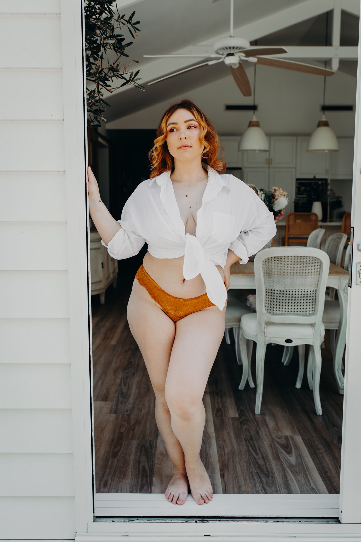 Modern boudoir photo in white crop shirt and copper underwear by glass door.