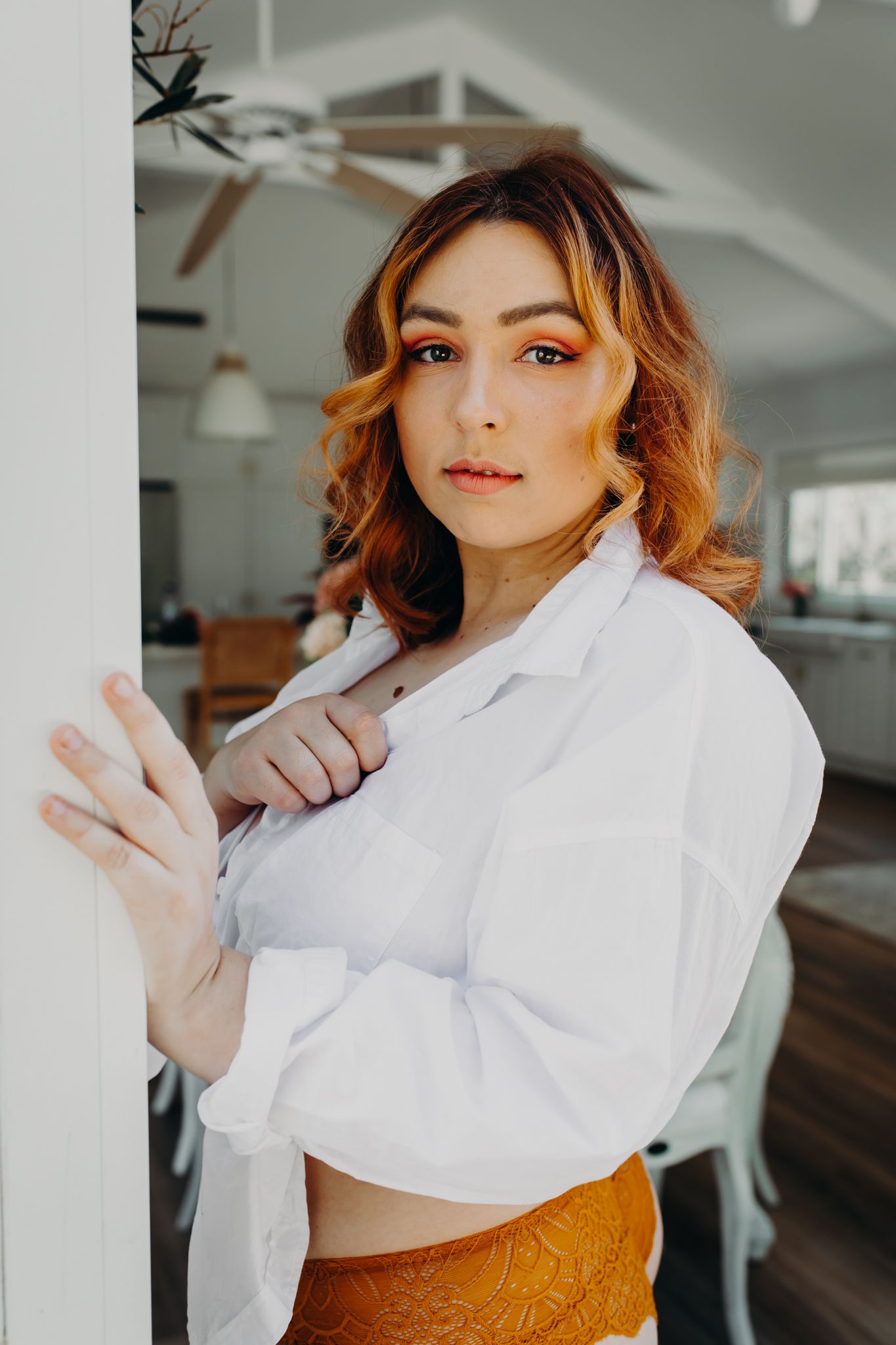 Elegant portrait in white button-down shirt and copper lace underwear against white wall.