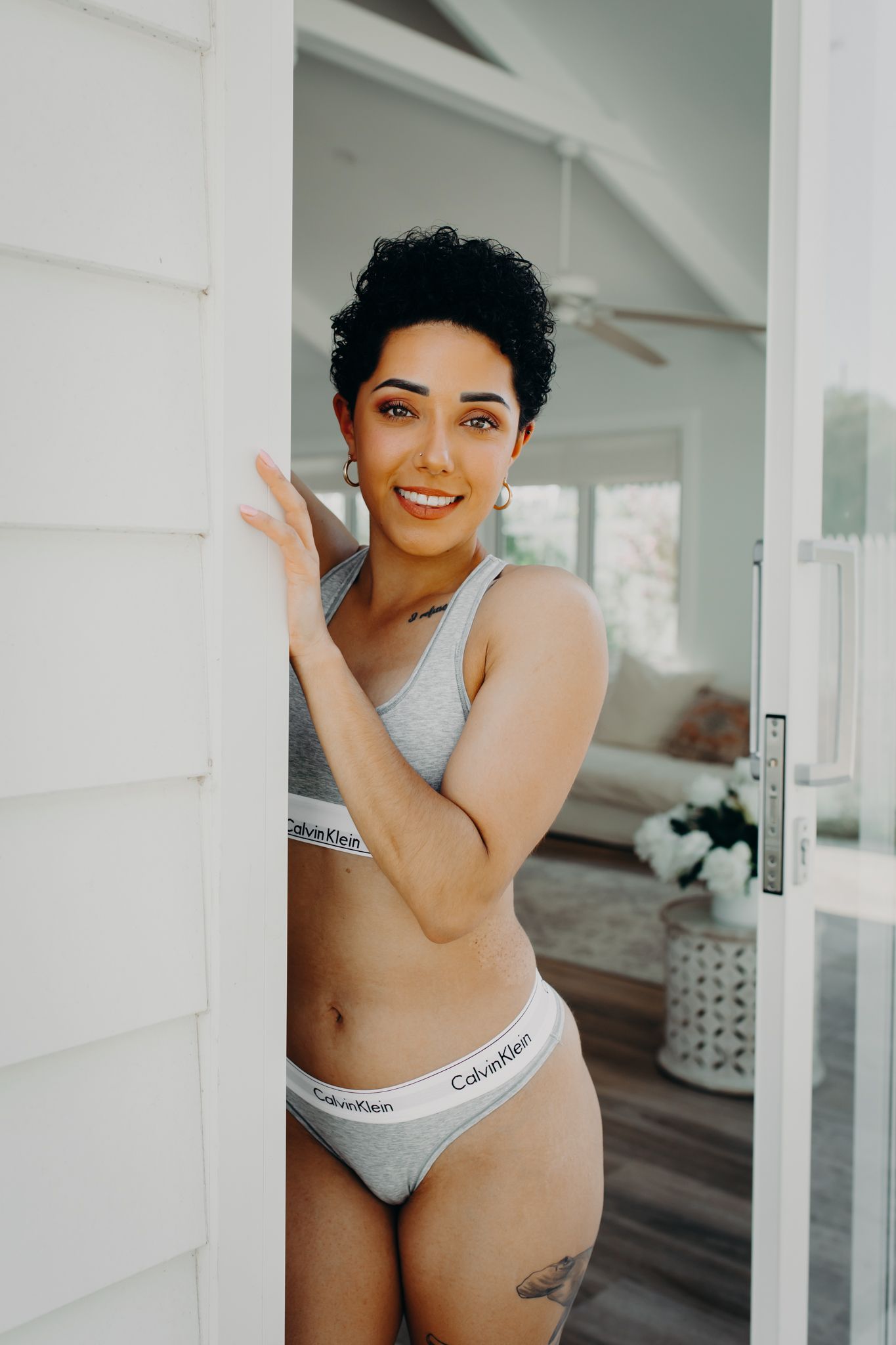 Model in grey Calvin Klein underwear set poses by doorway in bright setting.