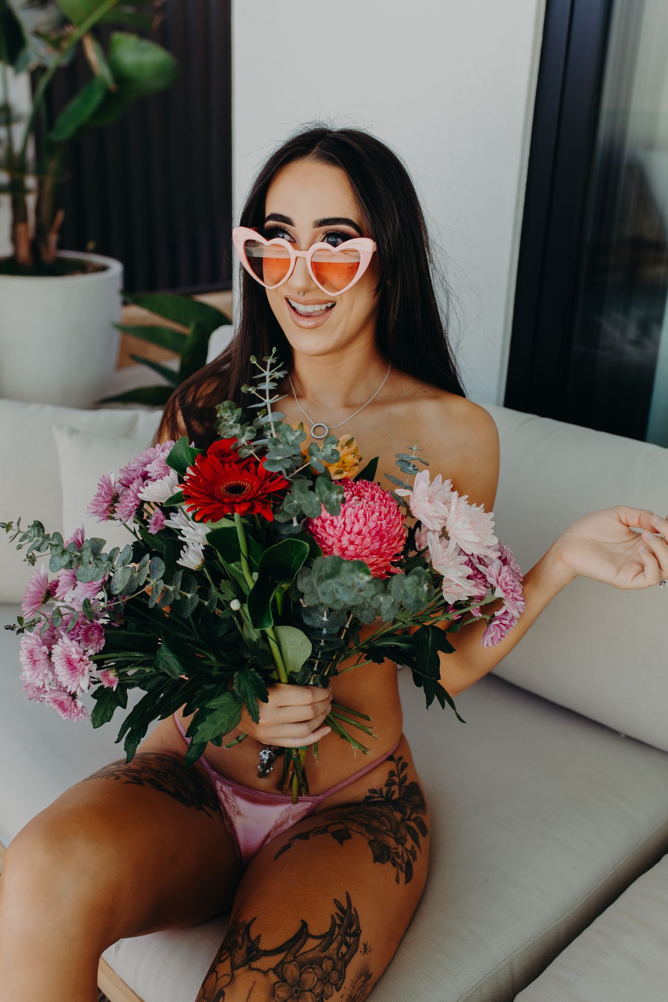 Person wearing heart-shaped orange sunglasses holding vibrant mixed flower bouquet.