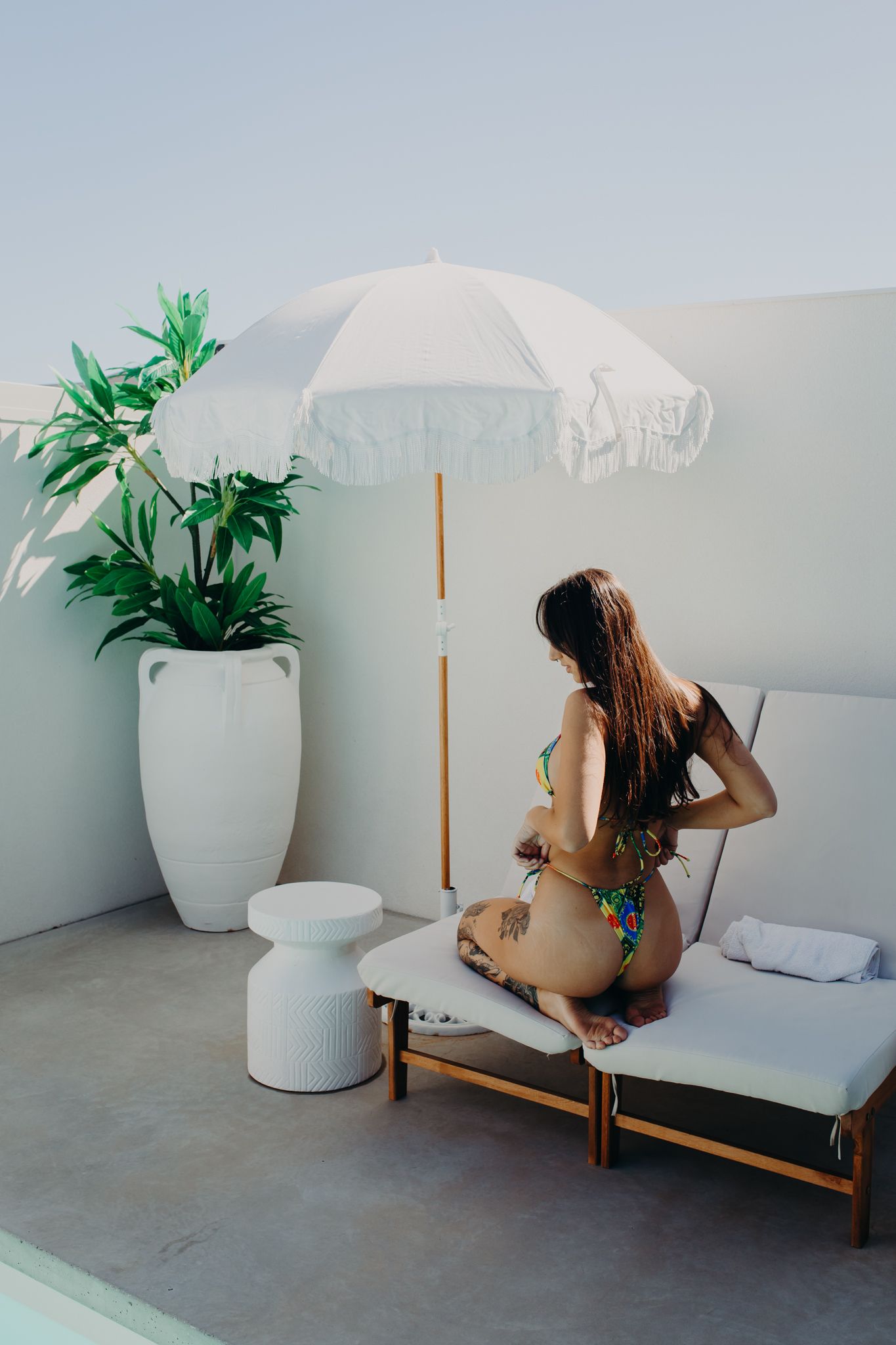 Minimalist outdoor lounge area with white umbrella and potted plant beside daybed.