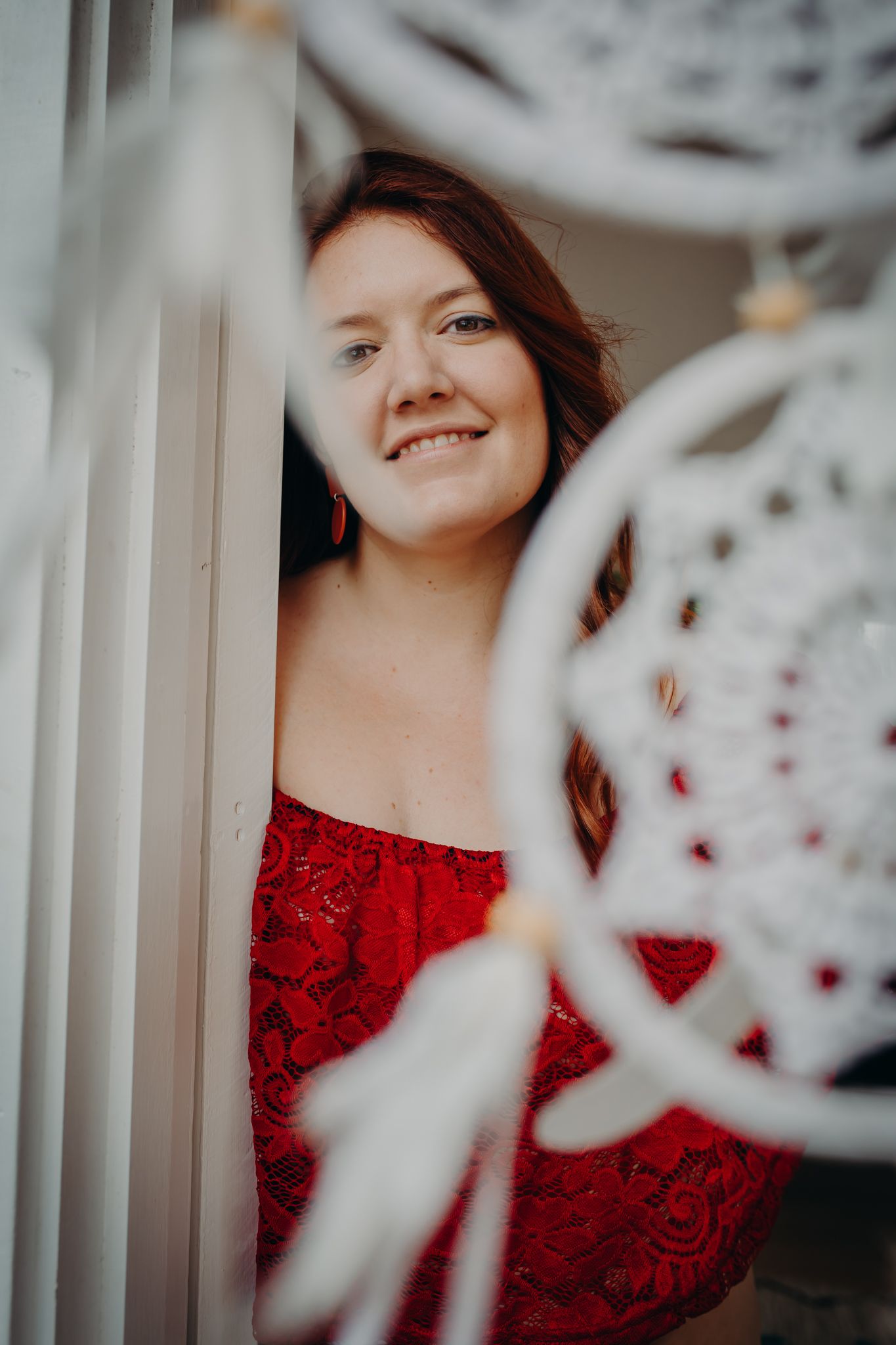 Artistic portrait through dreamcatcher with person in red lace top.