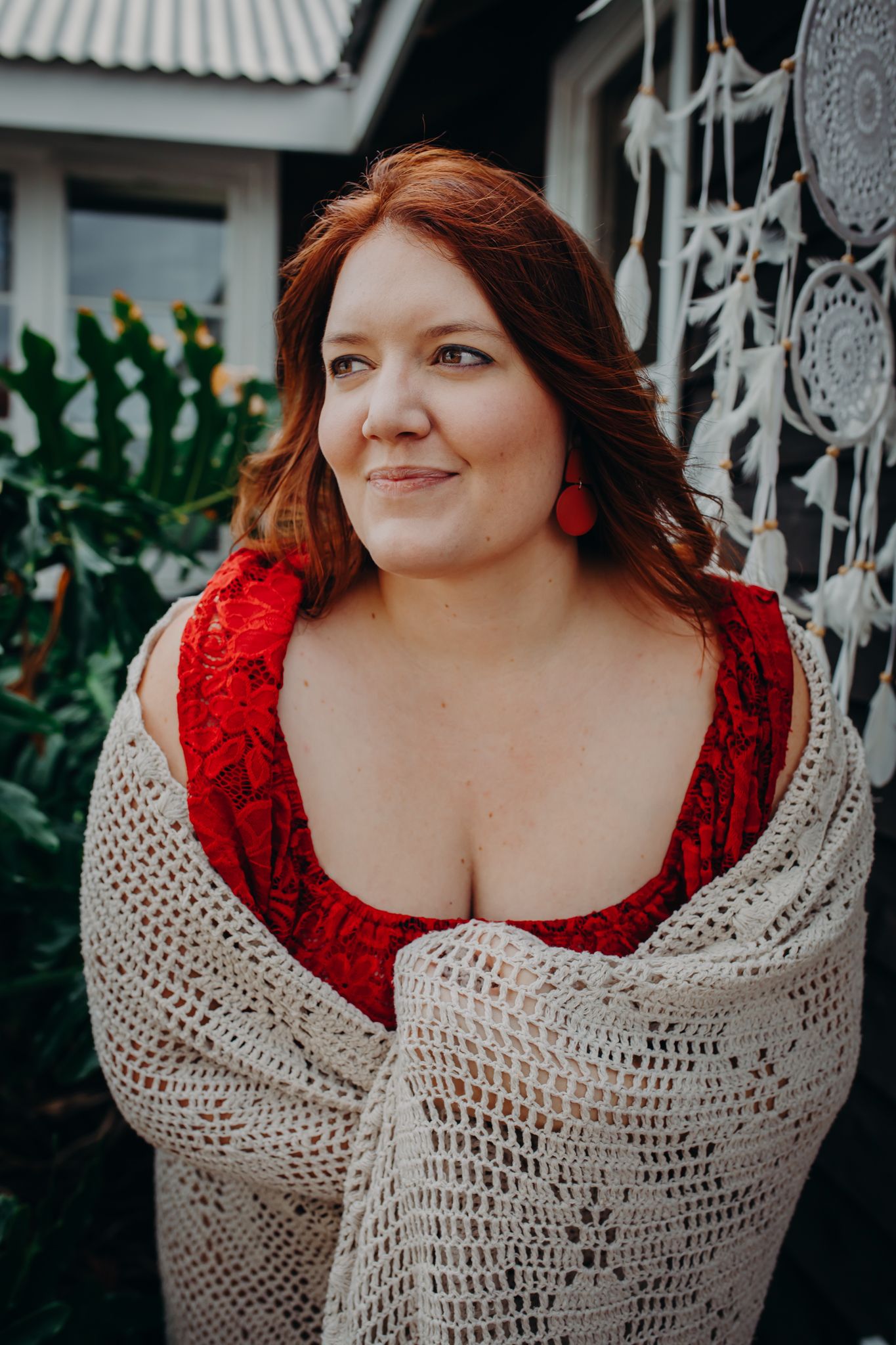 Portrait in red dress and cream knit cardigan against decorative wall backdrop.
