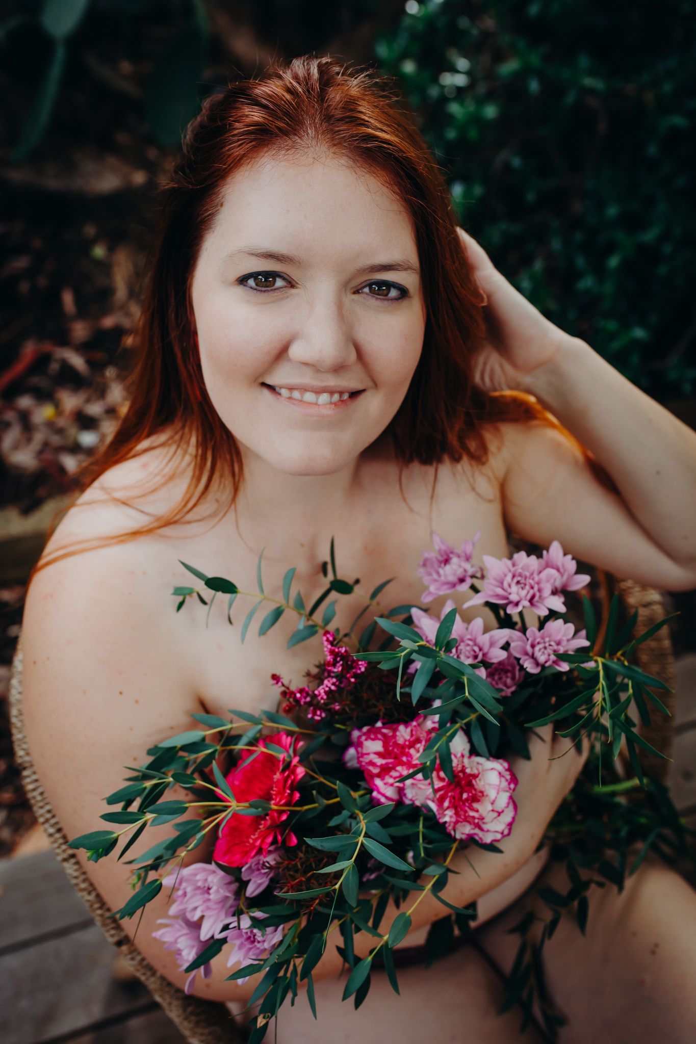 Outdoor portrait with vibrant flower bouquet featuring pink and red blooms against greenery.