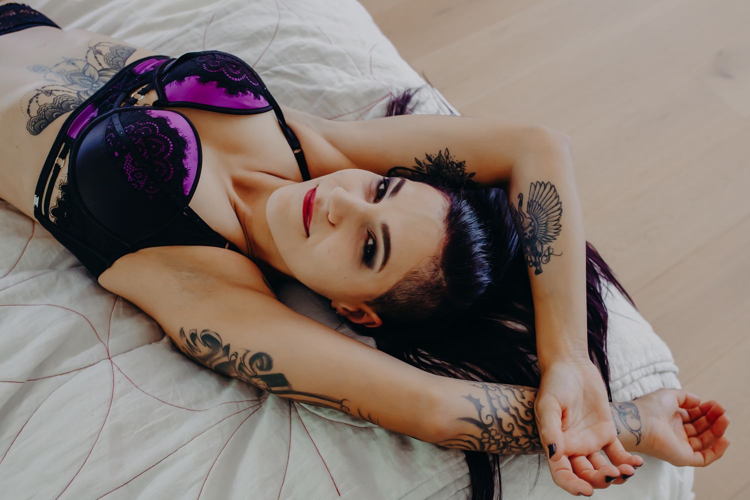 Model in purple and black lingerie reclines on white bedding with ski goggles.