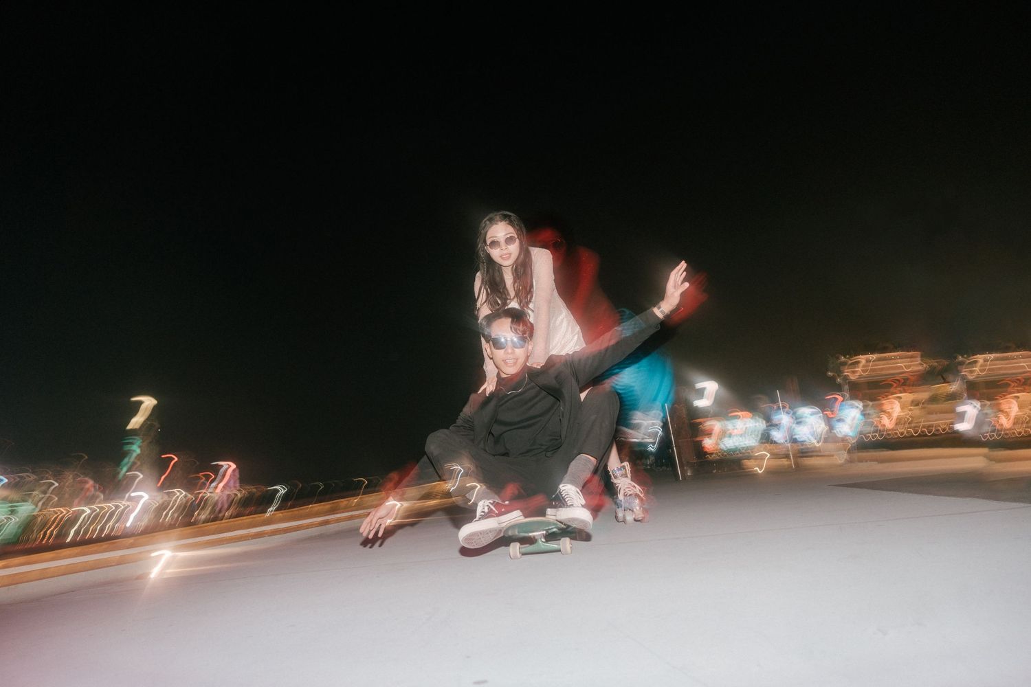 Action shot of people skateboarding at night with motion blur and city lights in the background.