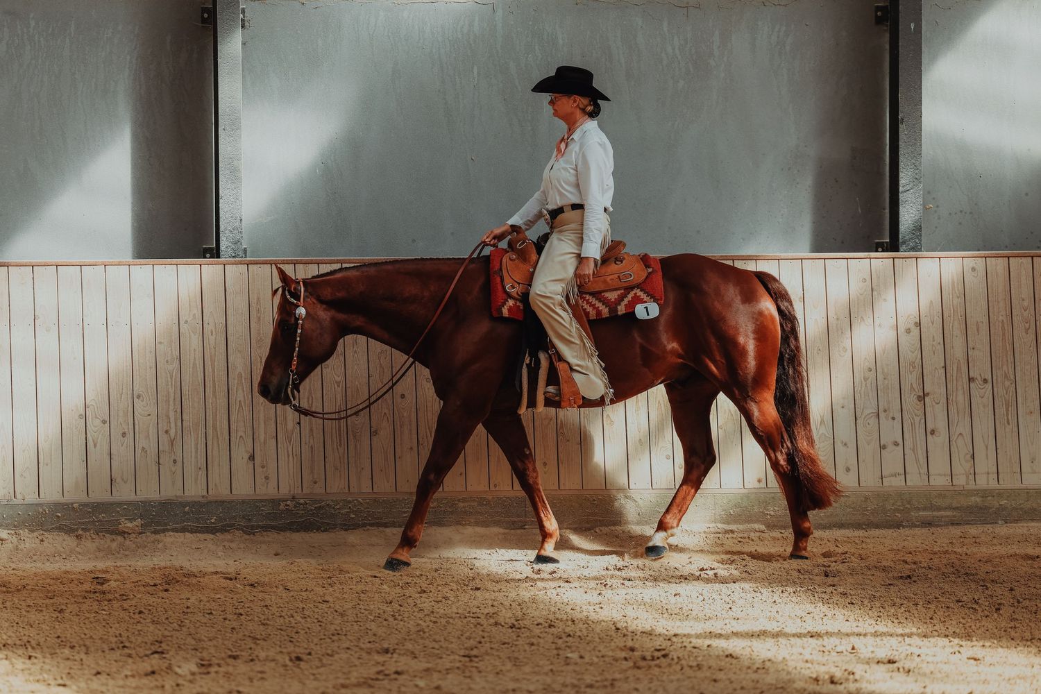 Rider demonstrates western horsemanship on a chestnut horse in an indoor arena.