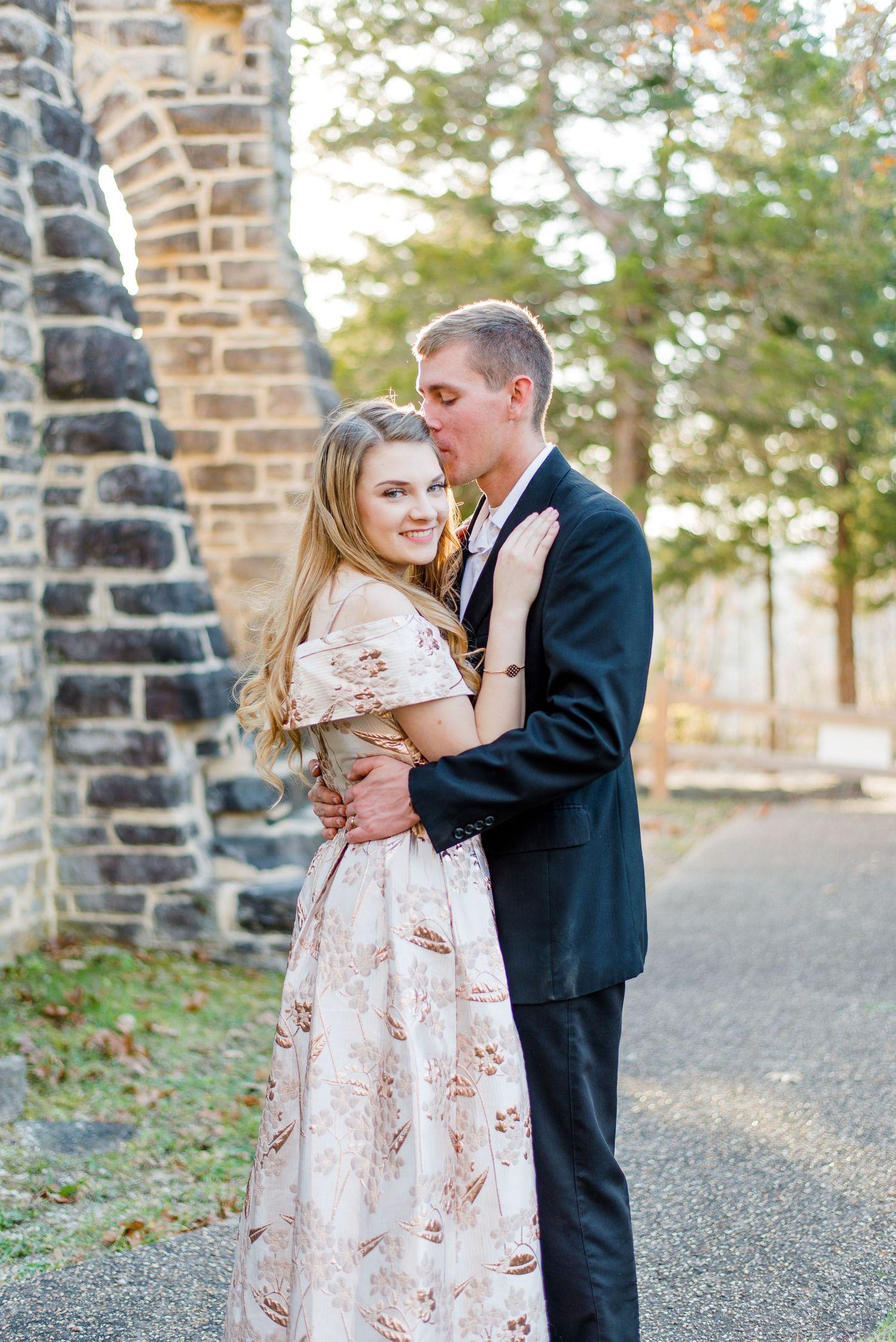 Couple embraces on stone pathway near brick wall during romantic outdoor photo session.