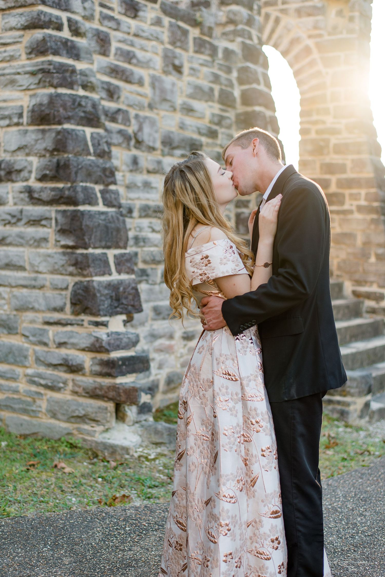 Two people share an intimate romantic moment embracing outside a historic stone church with sunlight peeking through an archway.