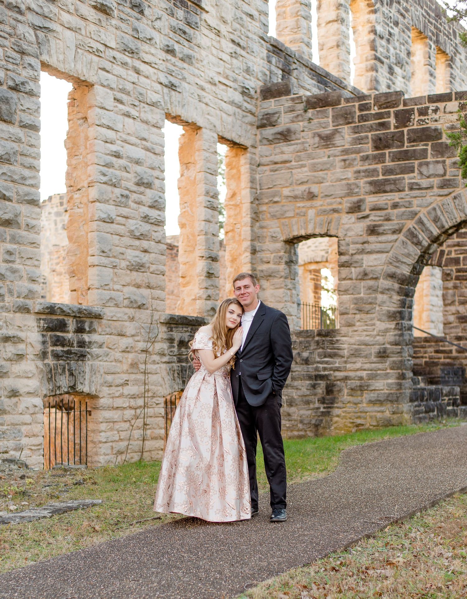 A couple poses together along a stone path inside historic ruins with elegant gothic arched windows and doorways.