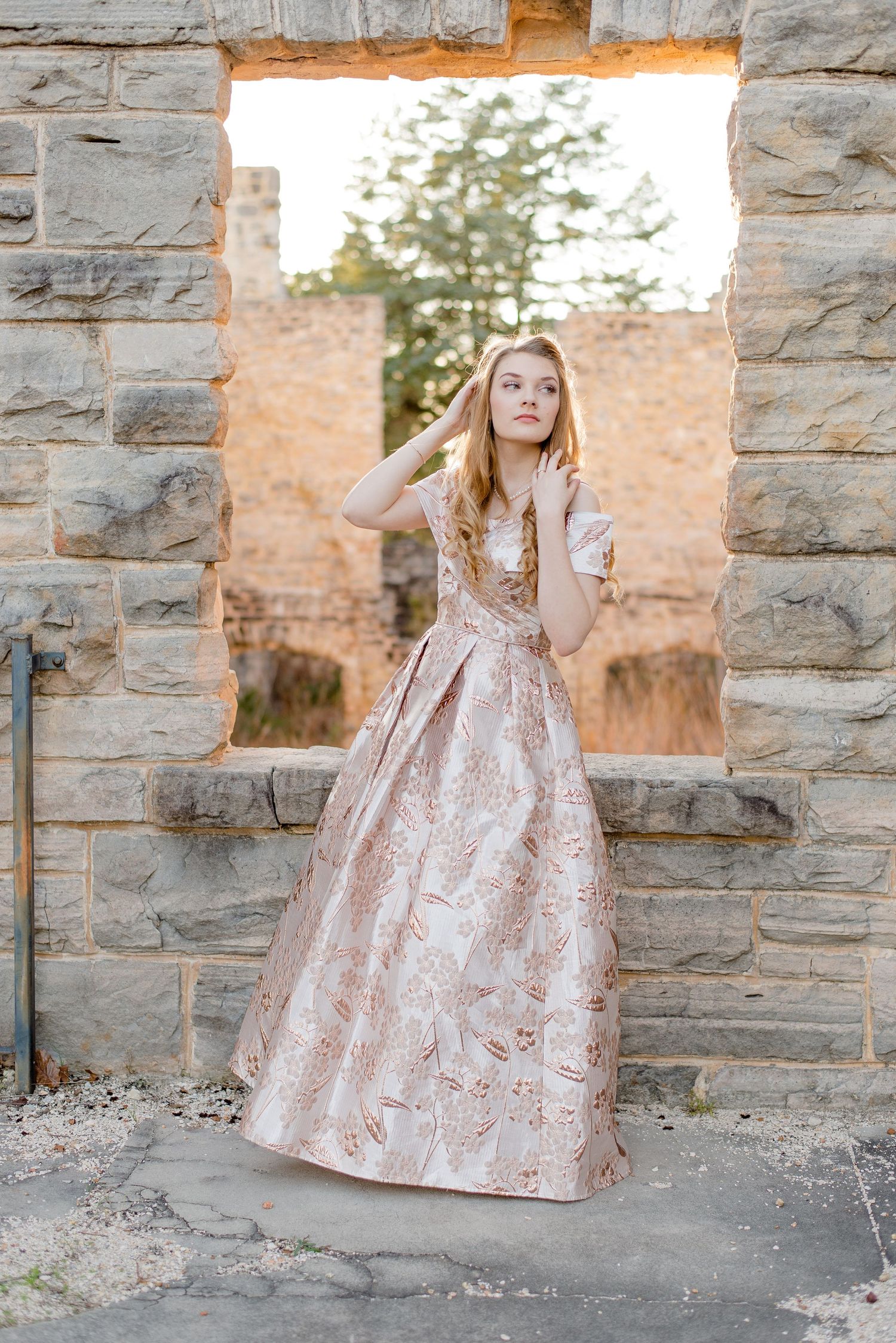 A formal pink brocade ball gown photographed in stone ruins against natural lighting.