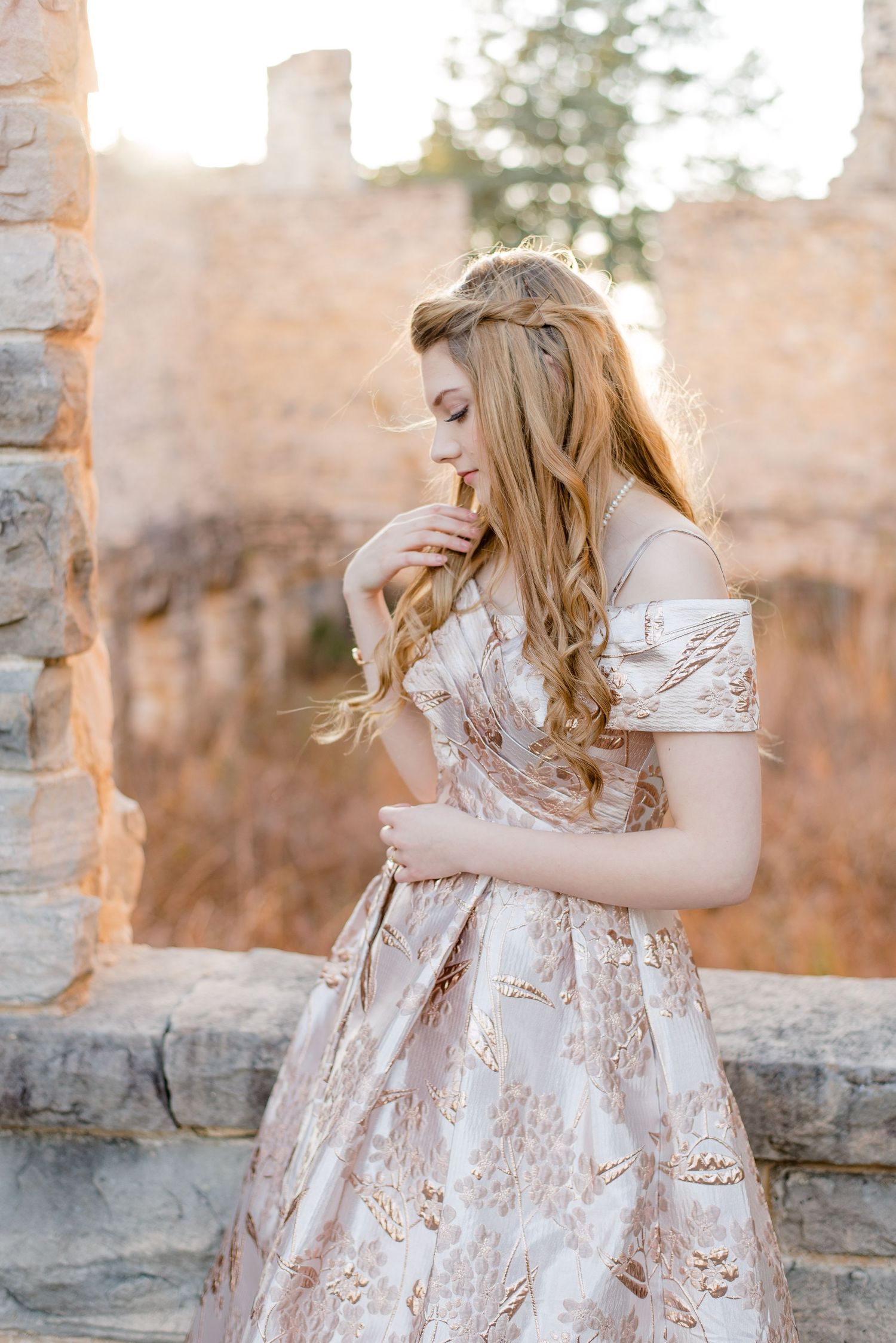 Romantic vintage-inspired gown with floral brocade pattern photographed against stone ruins at sunset.