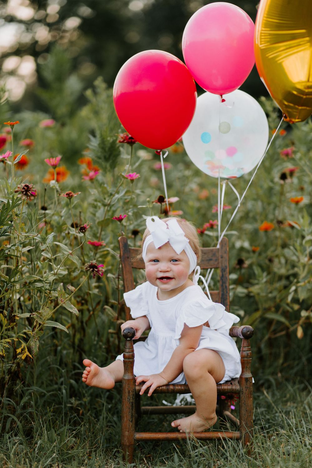 Festive birthday setup with balloons in wildflower field featuring wooden chair.