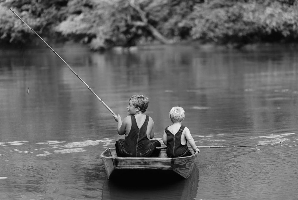 Vintage black and white photo of children fishing from small wooden boat.