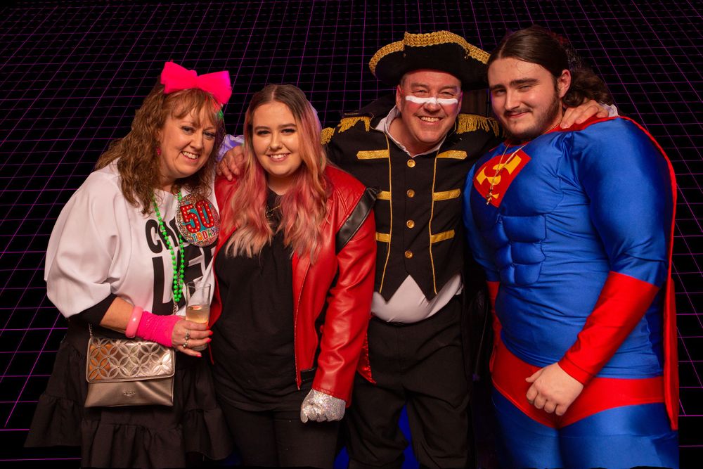 A group poses together at a costume party against a dark background.