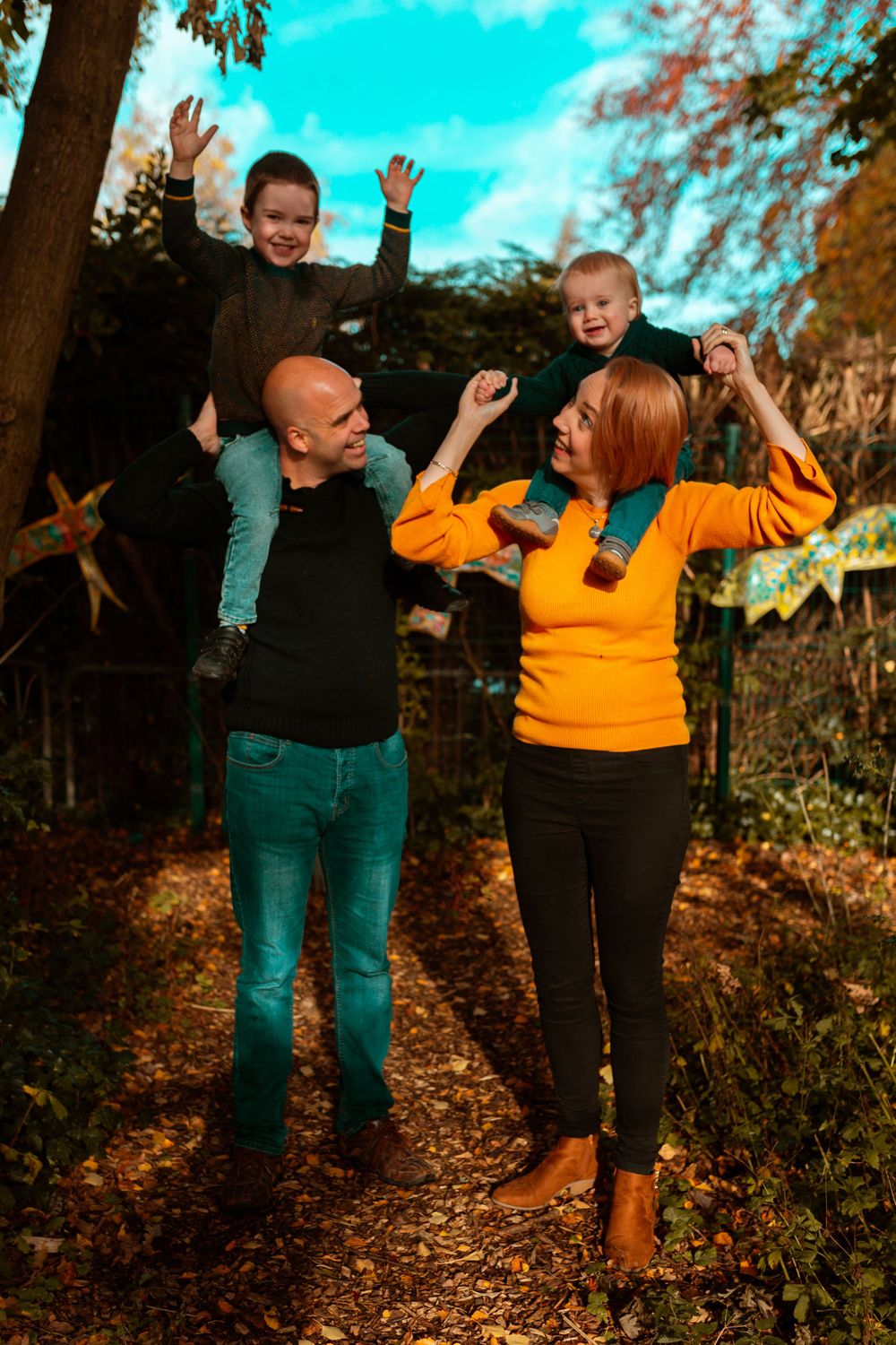 People in casual attire jumping and celebrating on an autumn path surrounded by trees.