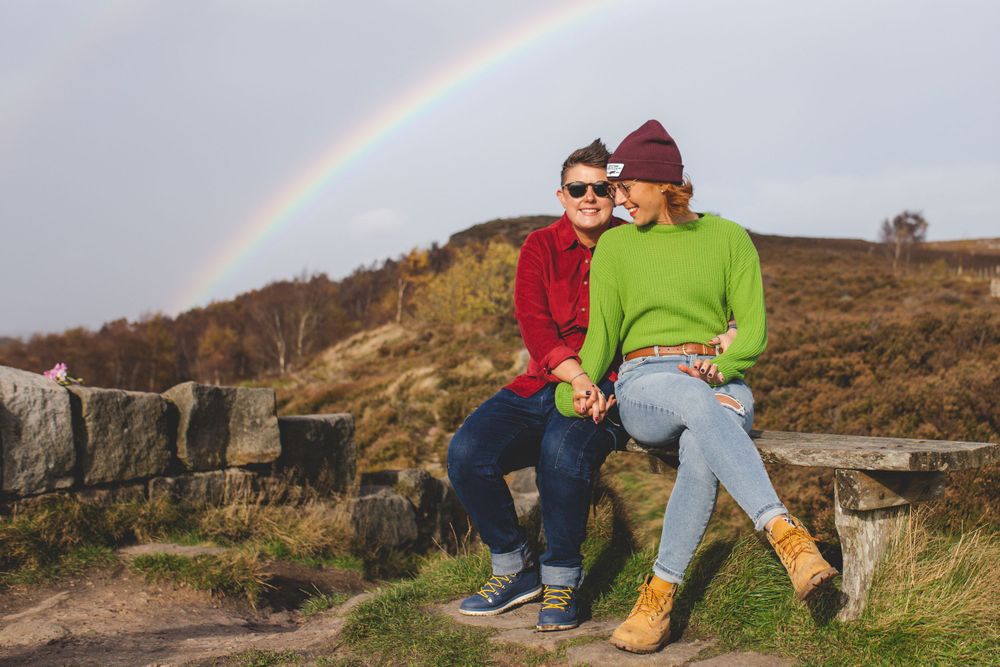 A rainbow arches across the sky over a scenic hillside landscape.