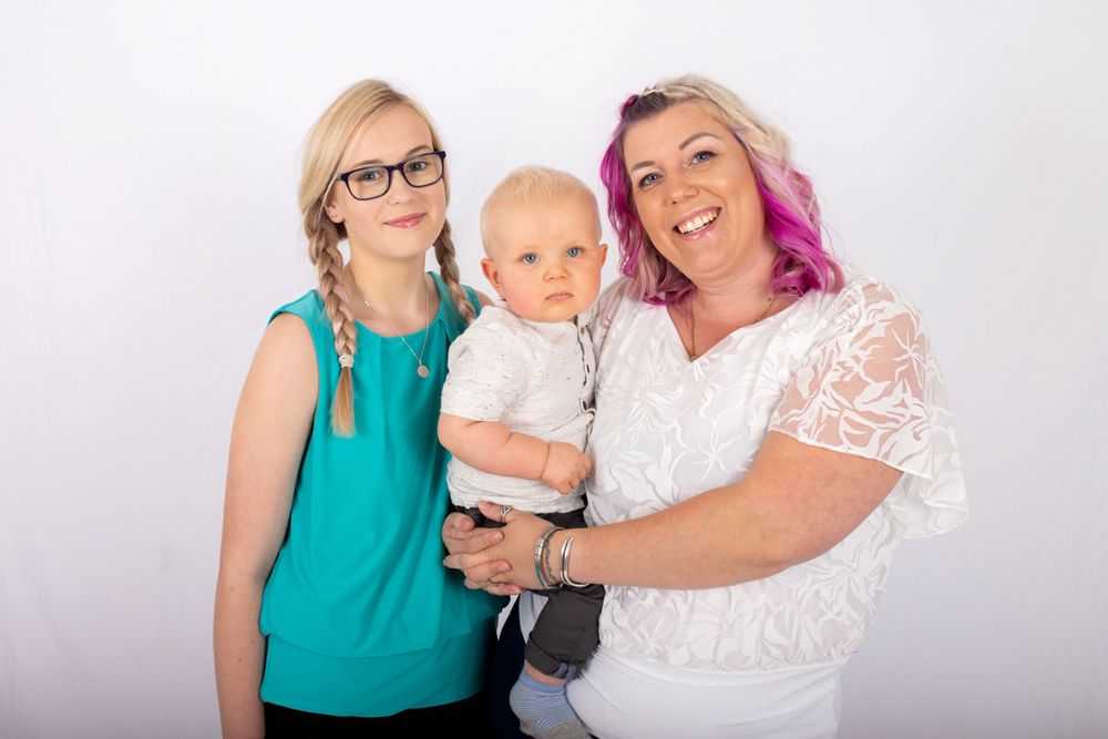 Family portrait of three people smiling together against light background.