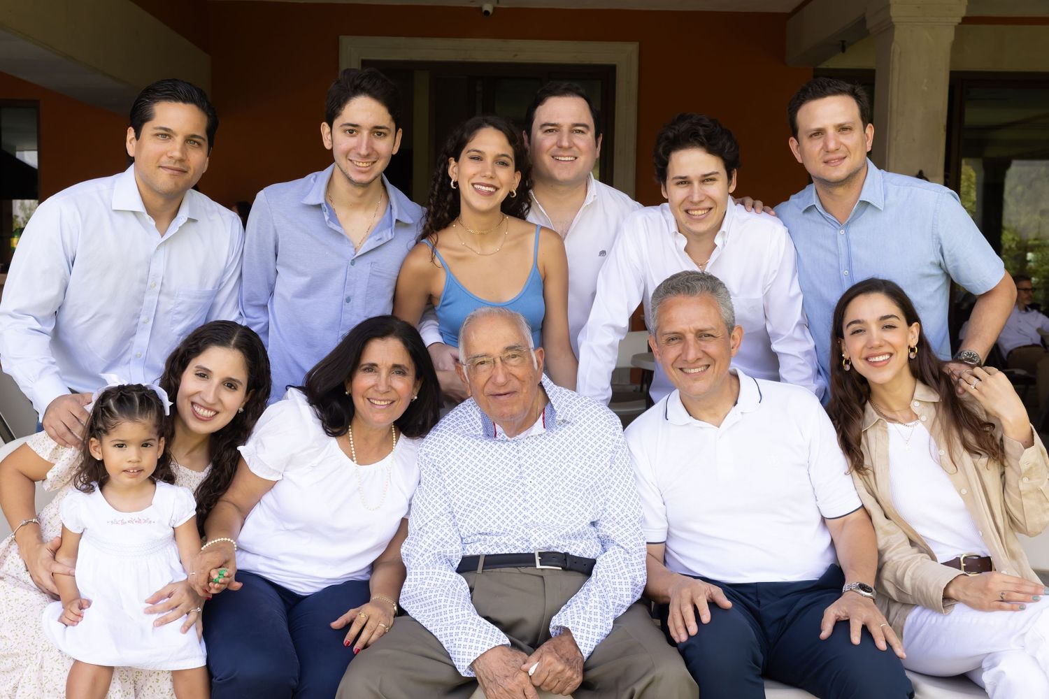 Large multigenerational family portrait posing together outdoors in coordinated white and blue outfits.