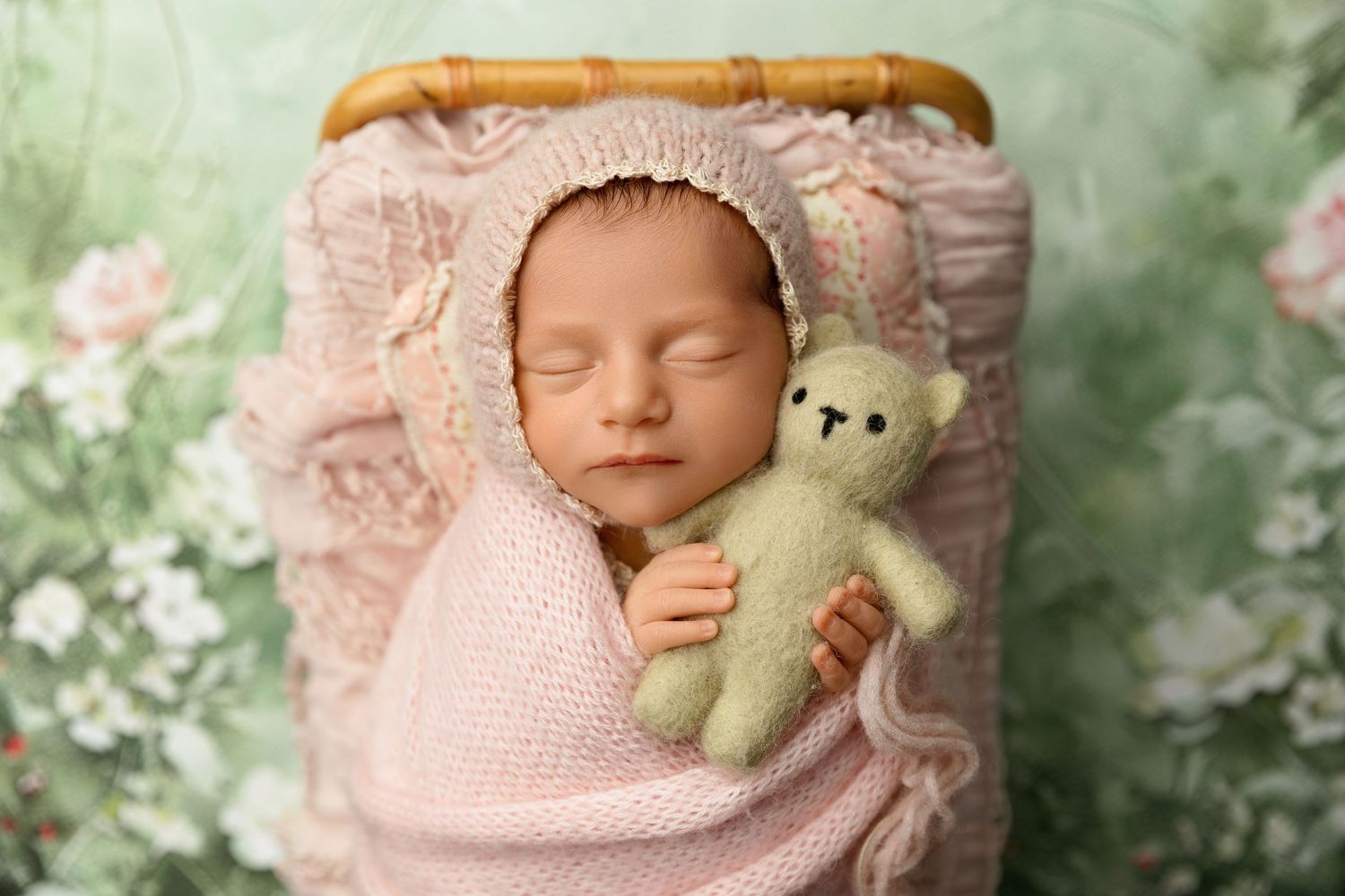 Newborn baby sleeping peacefully wrapped in pink with a teddy bear during a studio session in New Hampshire