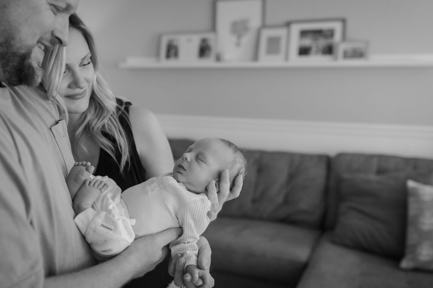 Black and white photo of parents tenderly holding their newborn baby in a cozy living room.