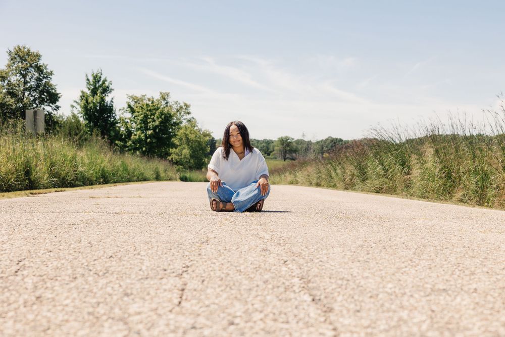 Casual portrait sitting on dirt path surrounded by summer meadow grasses.
