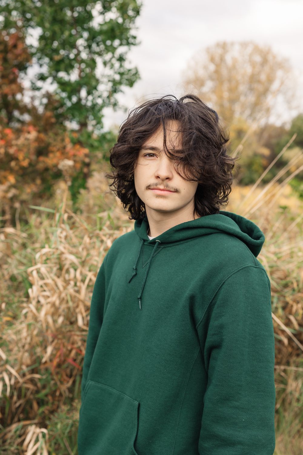 Person in green hoodie standing against autumn foliage background.