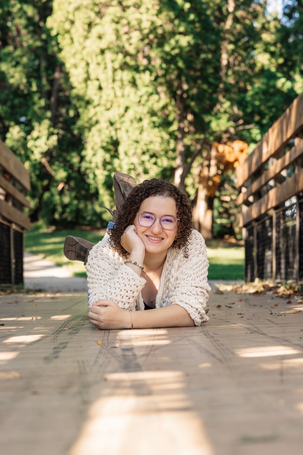 Person in white sweater lying on wooden deck with sunny forest background.