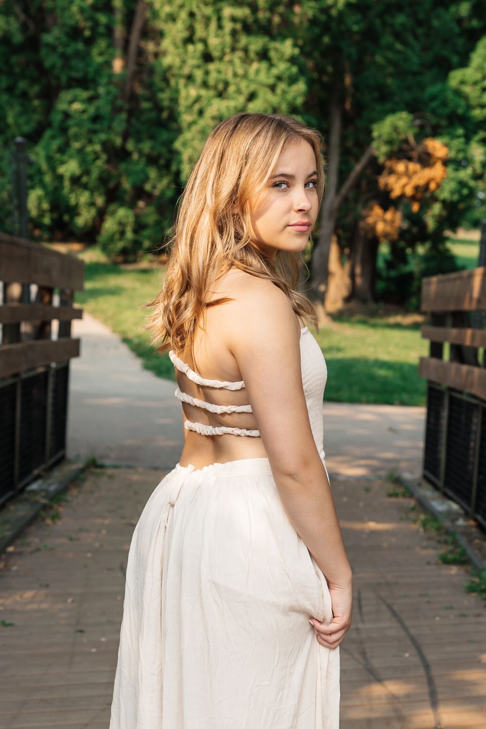 Elegant white dress with strappy back detail photographed on wooden bridge in park setting.
