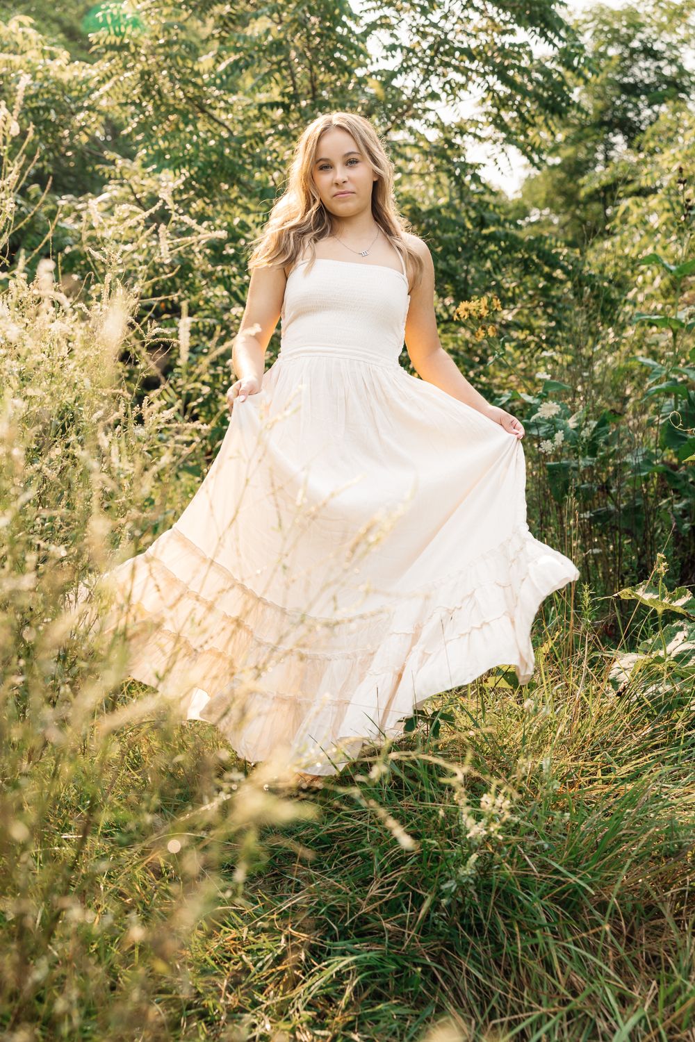 Flowing white dress captured in golden sunlight among tall grass and trees.