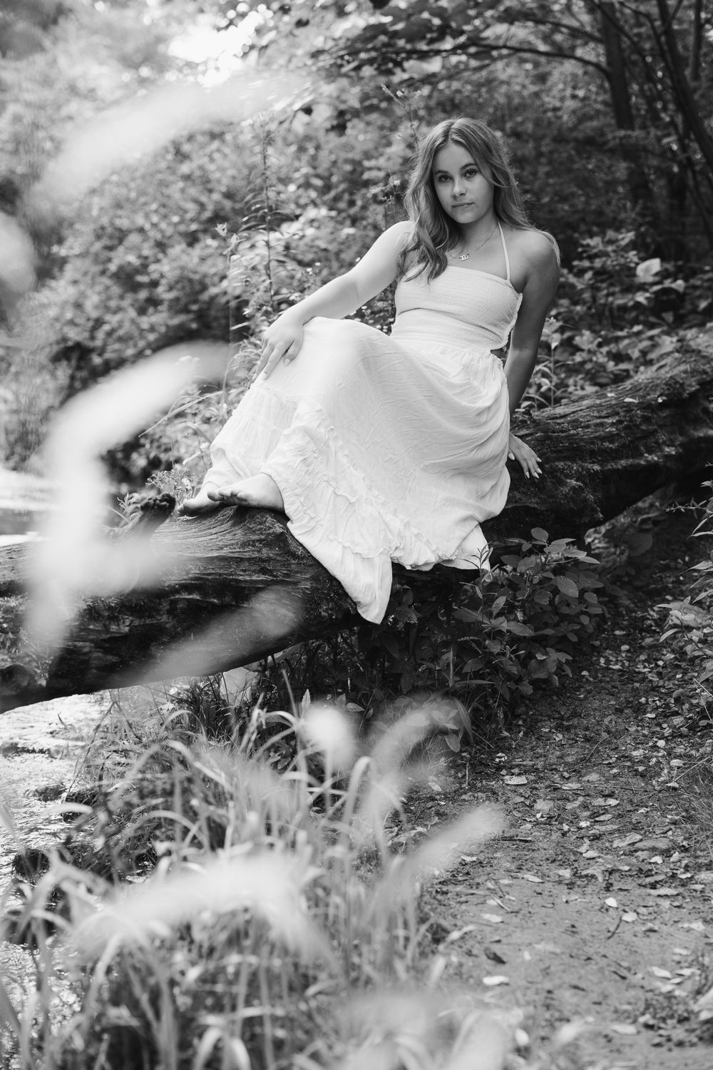 Black and white portrait of person in white dress seated on natural stone outcropping.