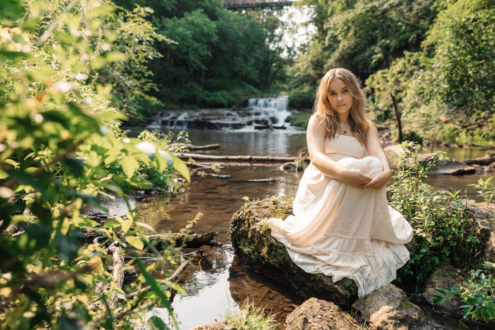 Dreamy portrait by cascading waterfall with white dress and natural scenery.