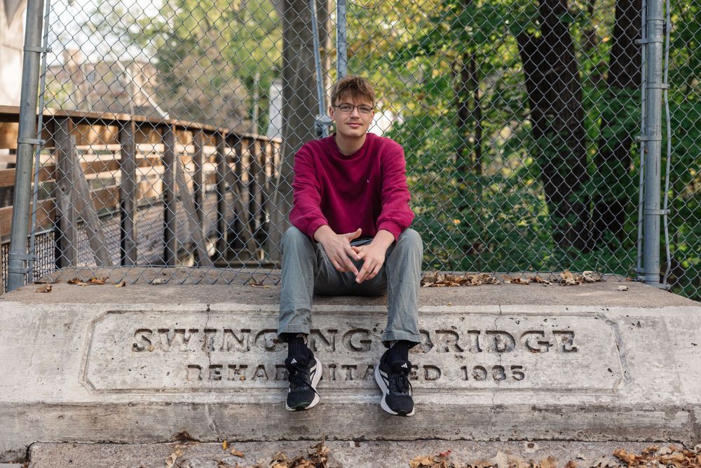 Someone sitting on historic swinging bridge marker in casual attire.