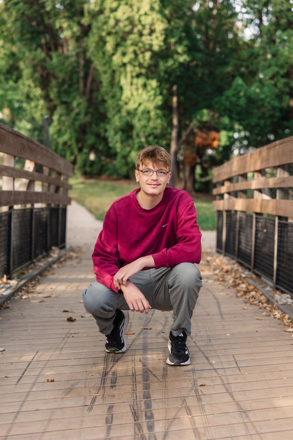 Person in red sweatshirt crouching on wooden bridge pathway.