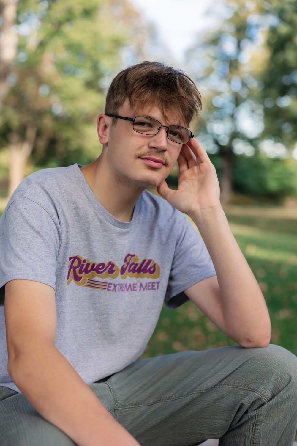 Person wearing River Falls t-shirt and glasses posing outdoors.
