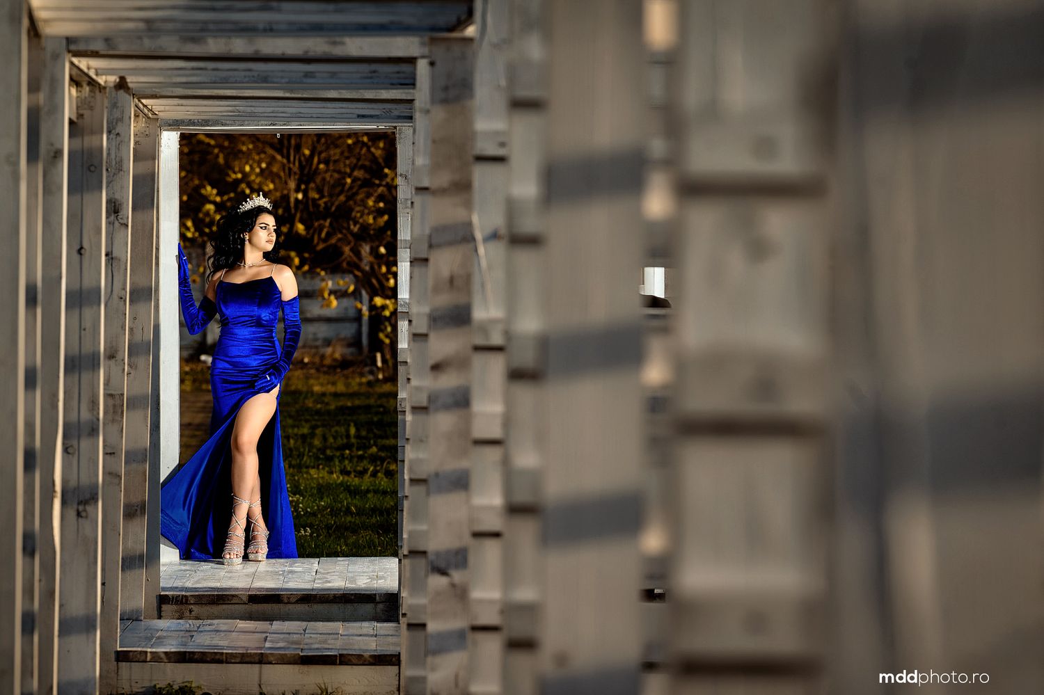 Model in blue dress framed through architectural columns with bokeh lights in background.