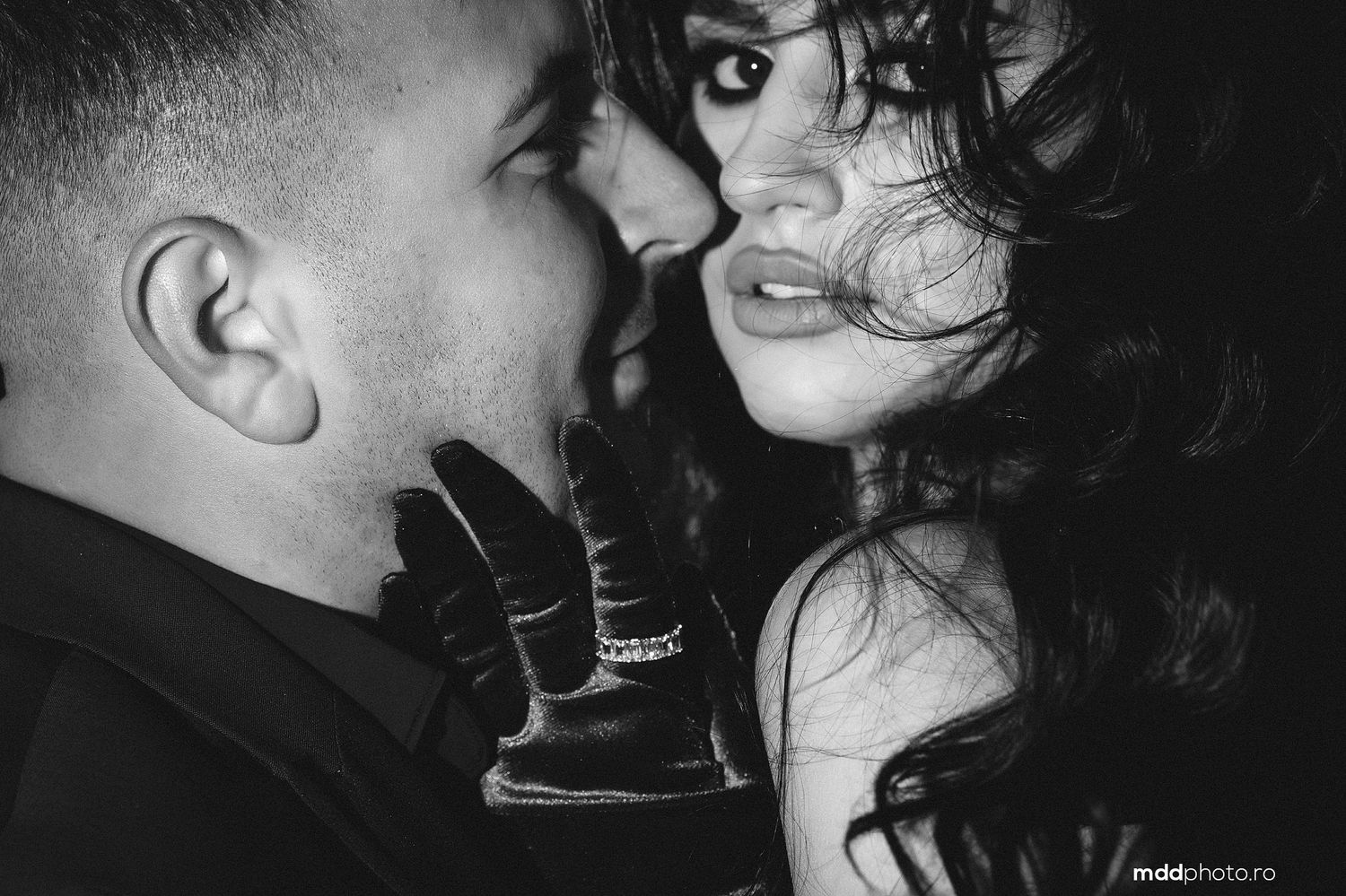 Black and white intimate portrait of a couple in a close embrace with dramatic lighting and shadows.