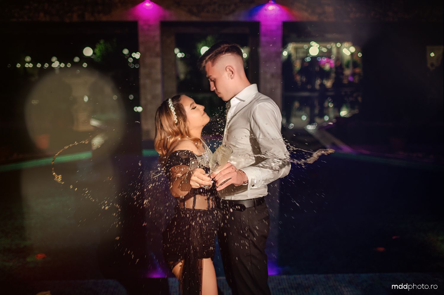 Couple slow dances at dimly lit event venue with purple lighting and glowing effects in background.