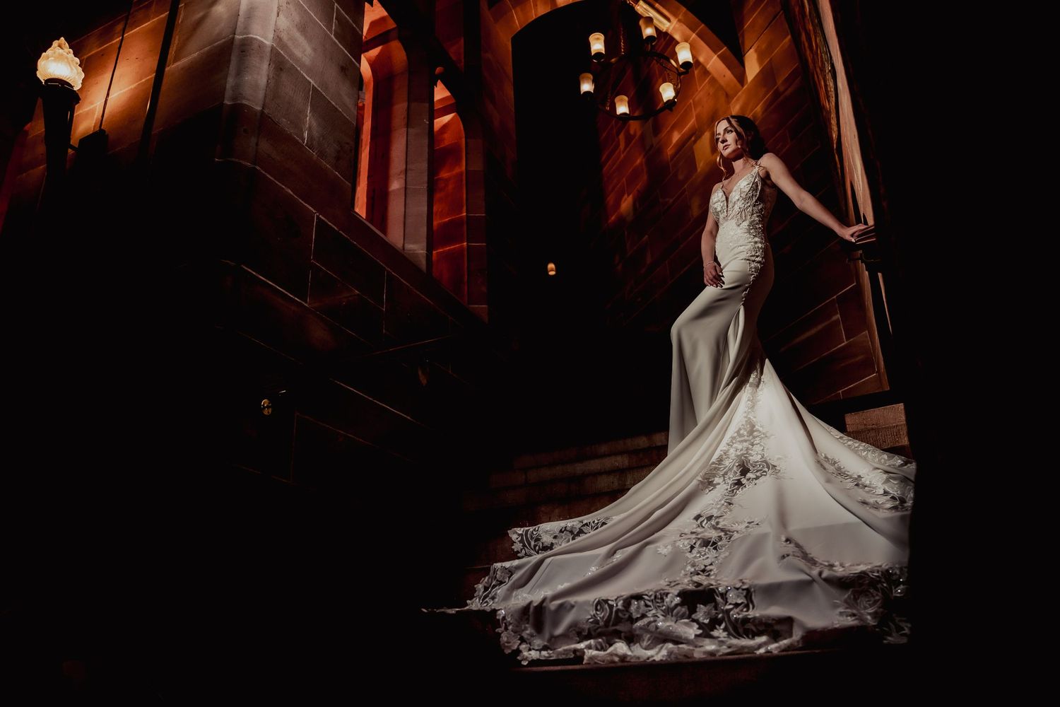 Dramatic bridal portrait featuring a flowing lace wedding gown in gothic architecture setting.