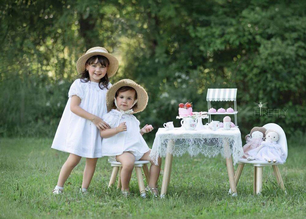 Children enjoy a charming outdoor tea party picnic with white decor and vintage elements on a sunny summer day.