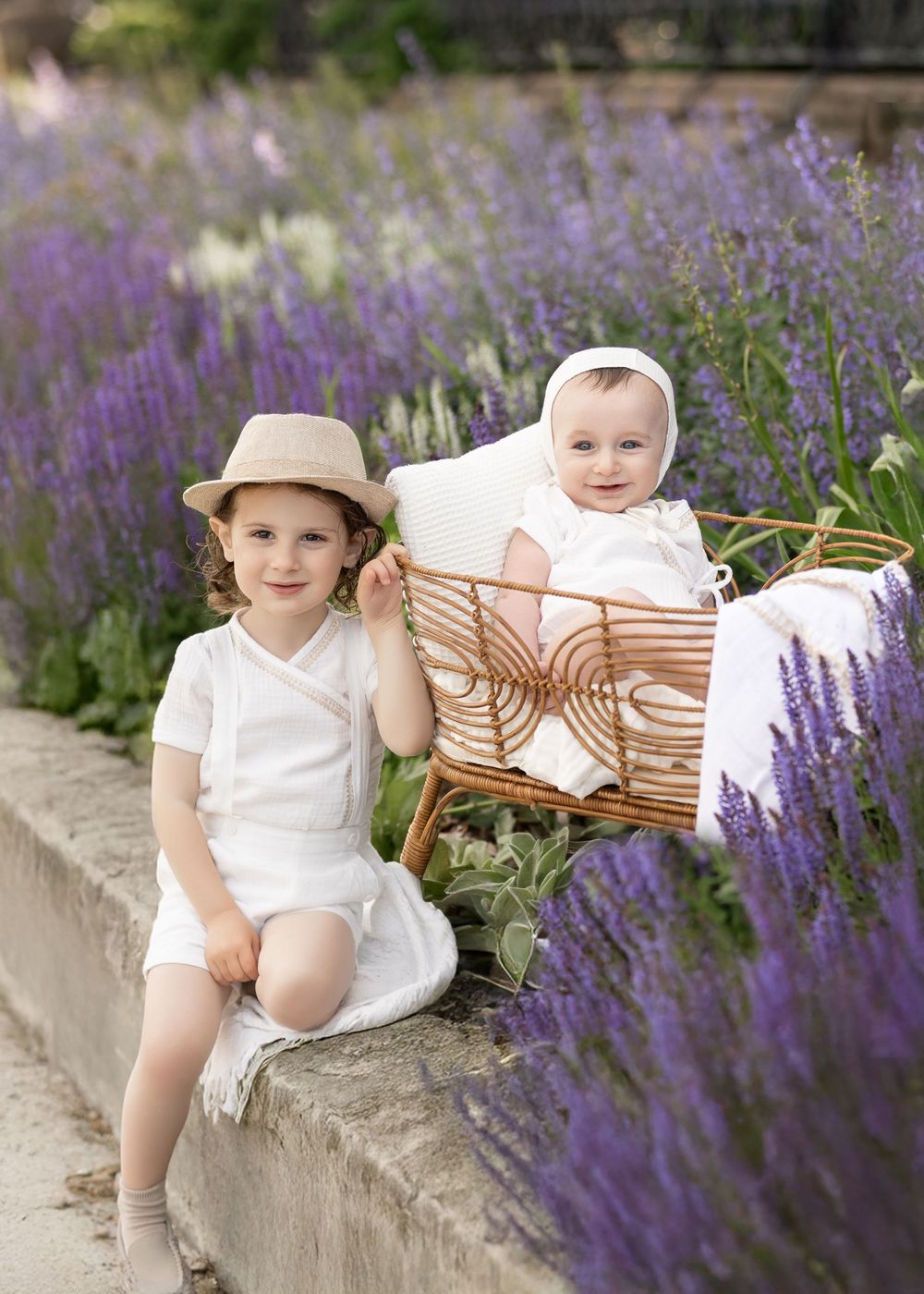 Children dressed in white sitting together among blooming purple lavender flowers in a summer garden scene.