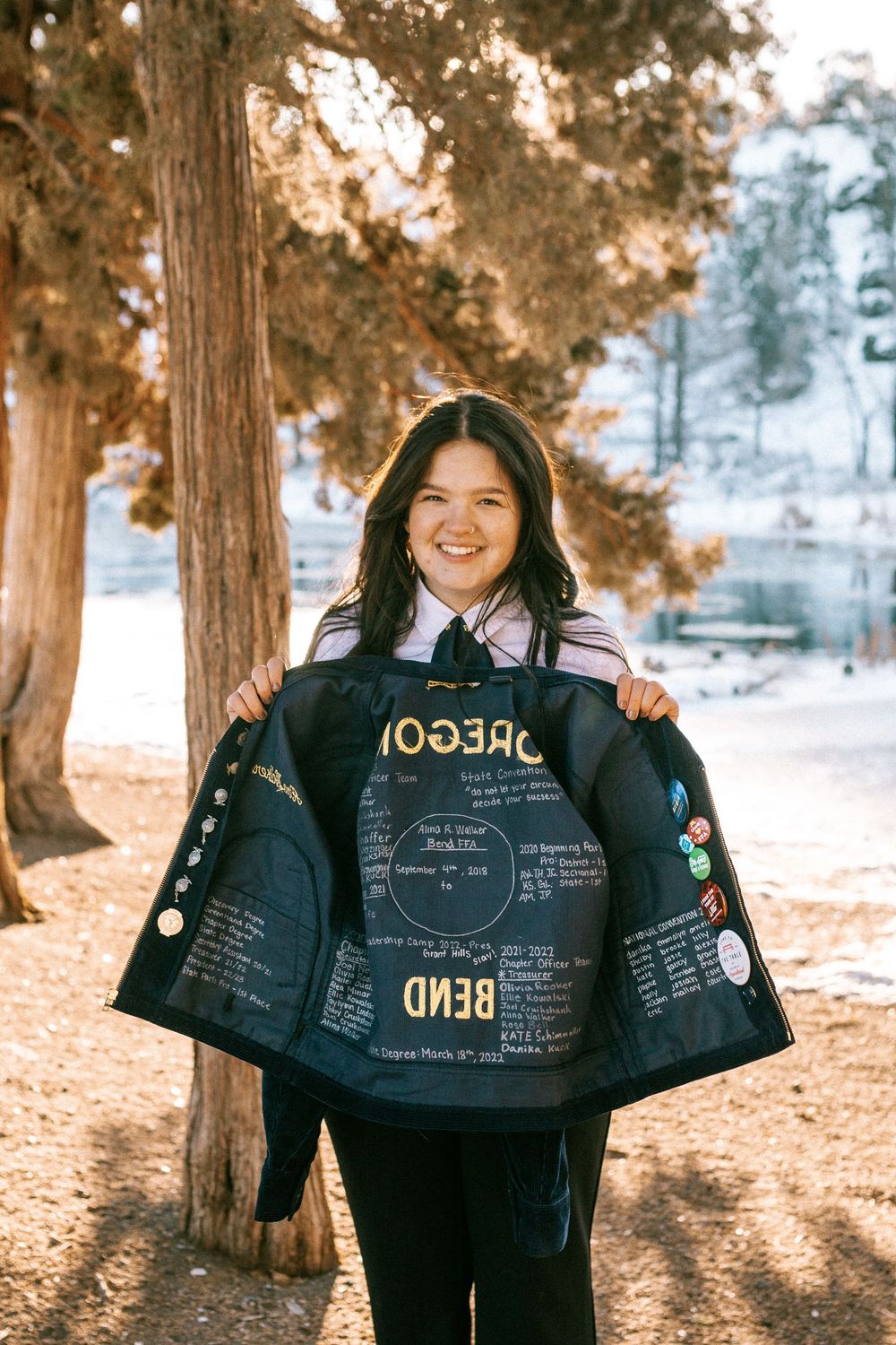 A person outdoors in winter displays the inside of a decorated jacket featuring text and designs against snowy trees.