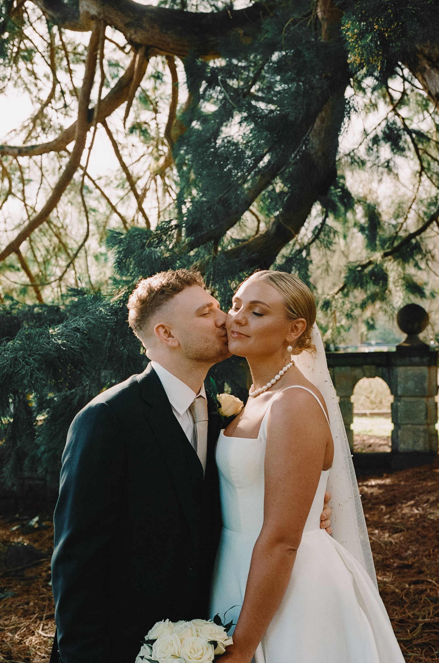 A joyful wedding couple walking hand in hand under weeping willow trees.