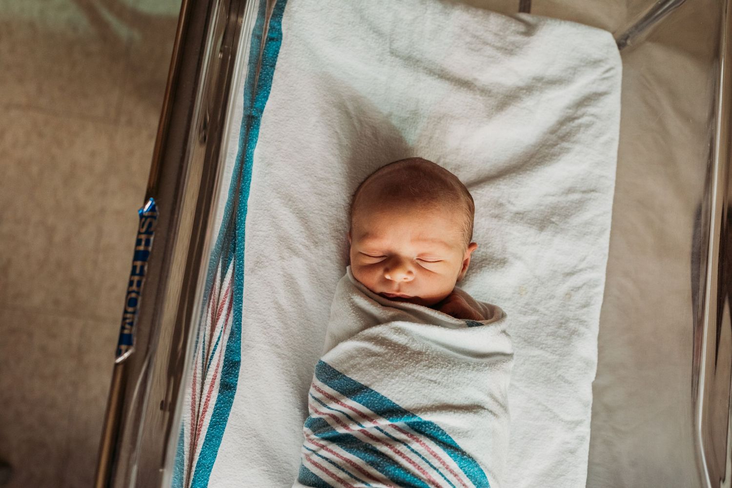 Sleeping newborn swaddled in white and blue striped blanket.
