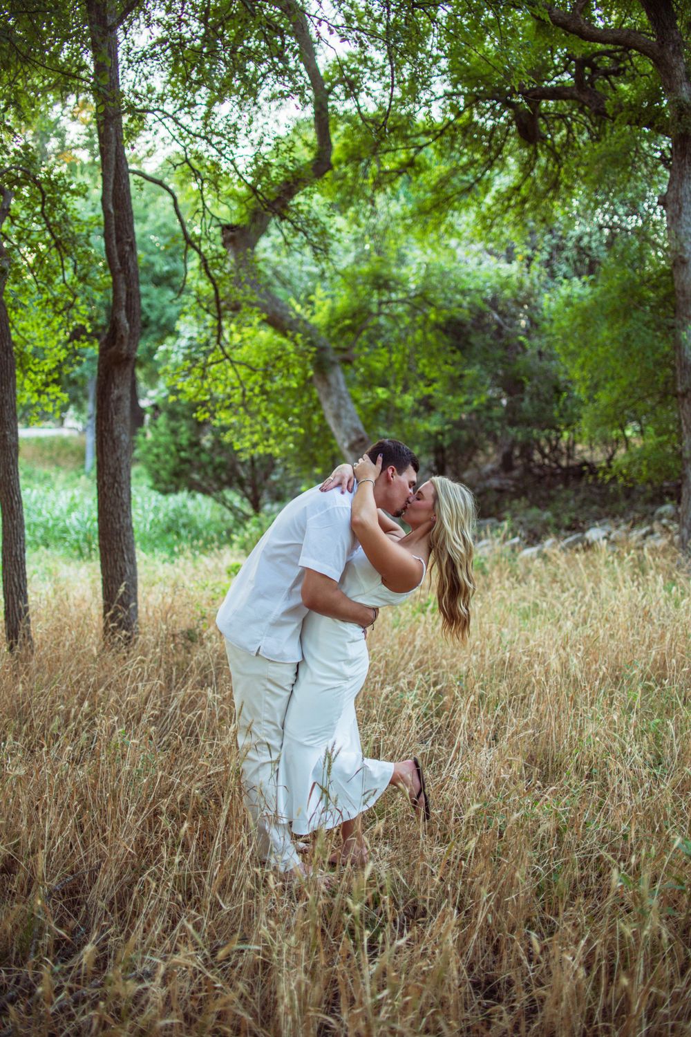 Couple in white clothing sharing romantic moments in a rustic field with tall grass.