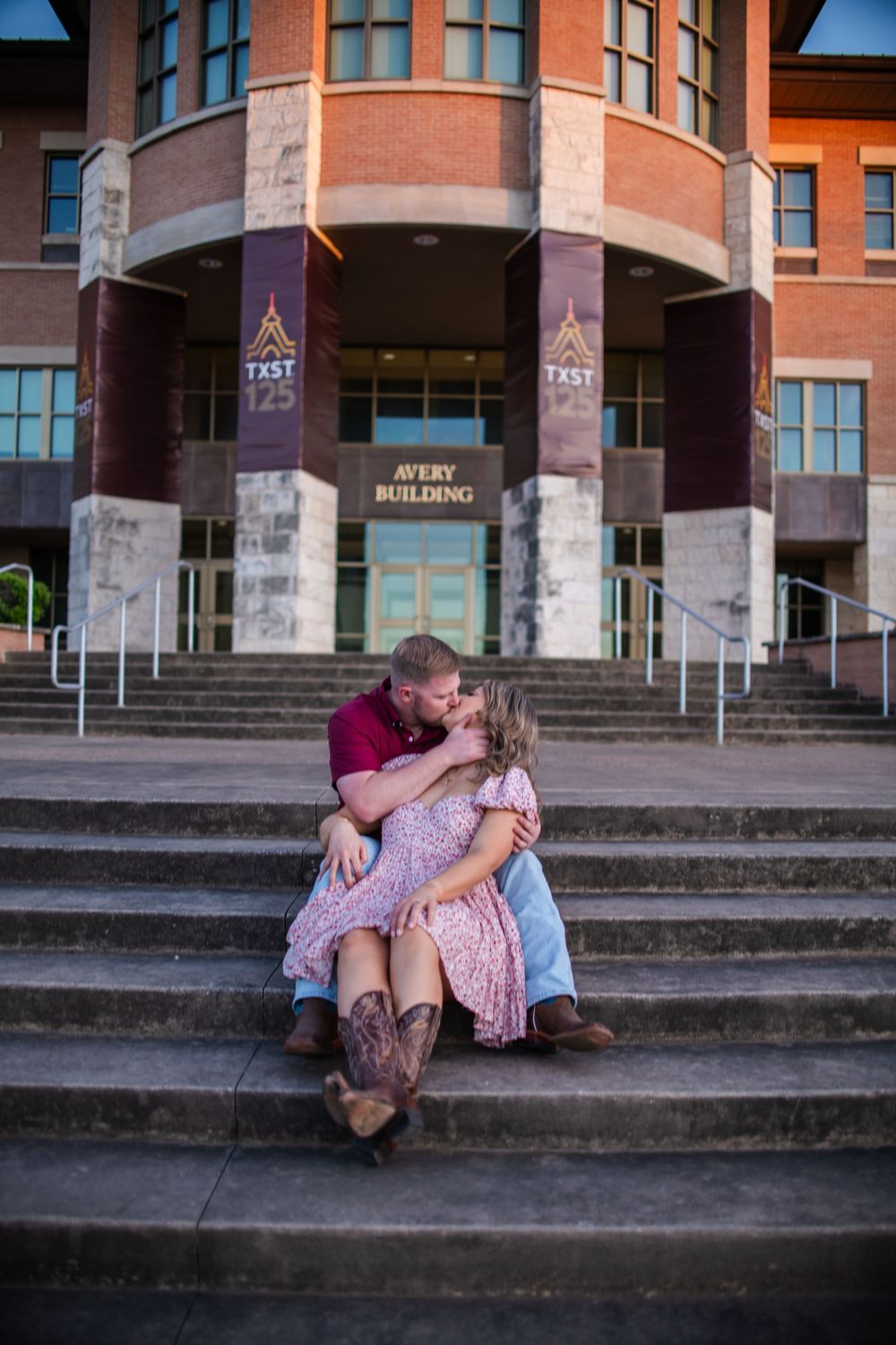 A couple shares an intimate moment on concrete steps outside a brick building.