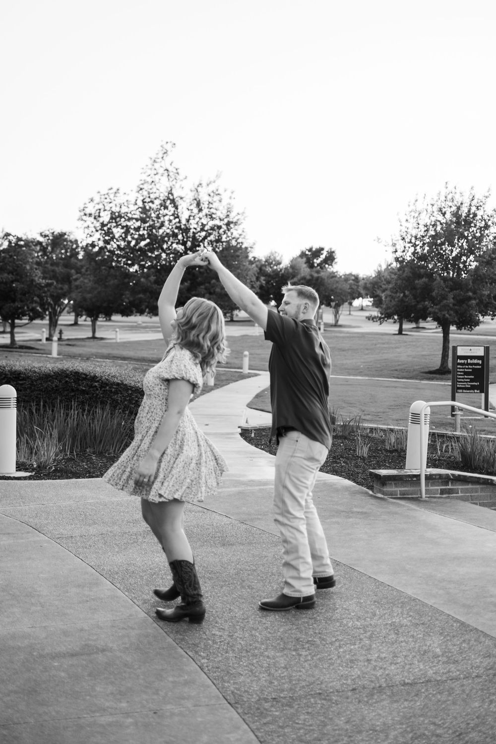 A couple dances and twirls together on a concrete pathway in black and white.