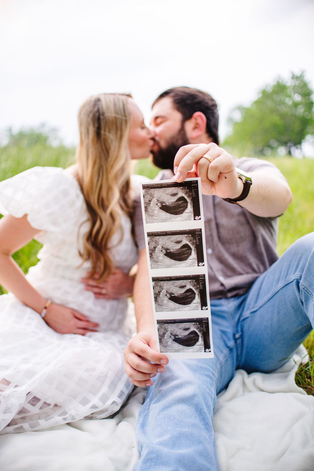 Couple shares tender moment while holding ultrasound photos in outdoor setting.